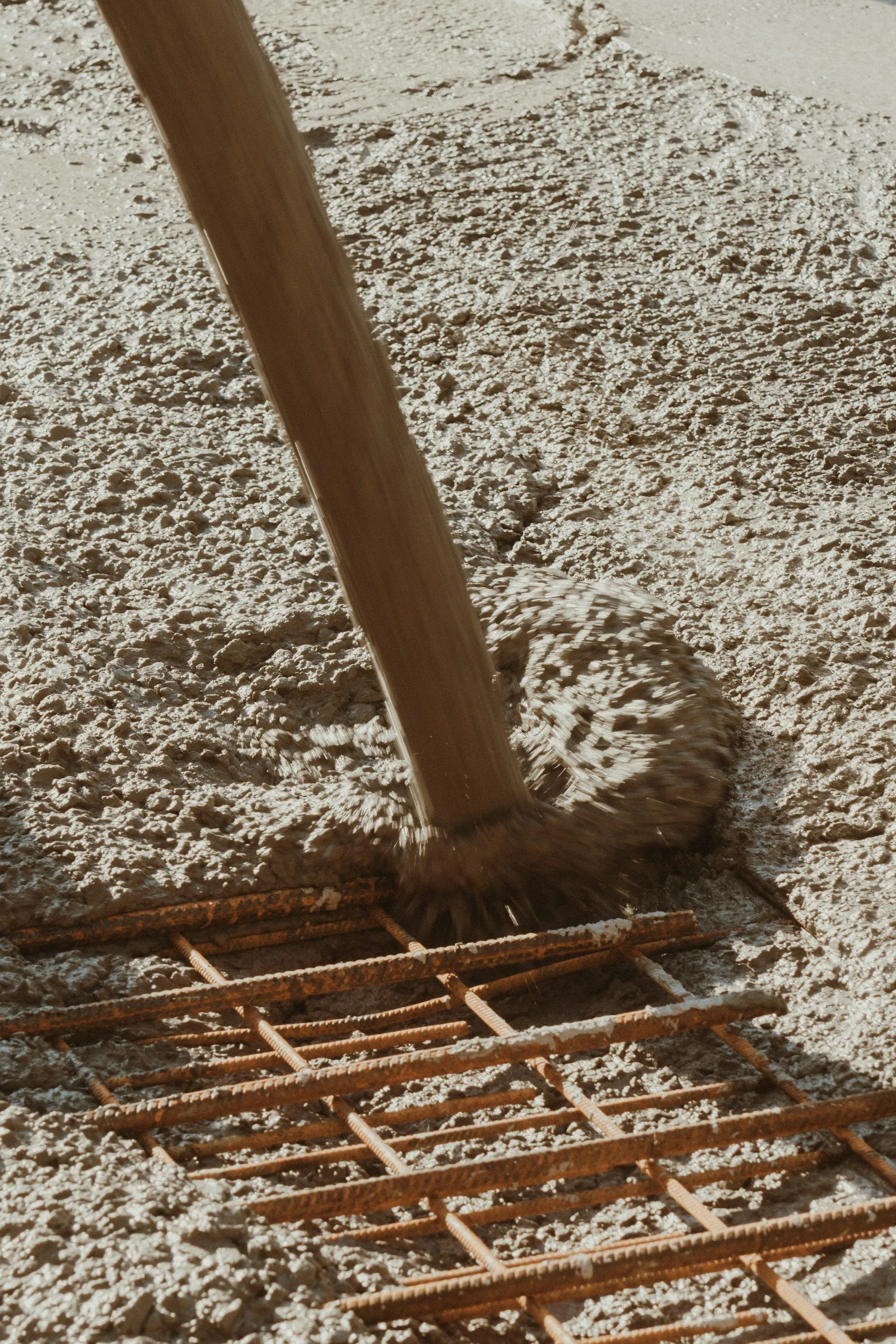 Worker spreading wet concrete with a rake over rebar